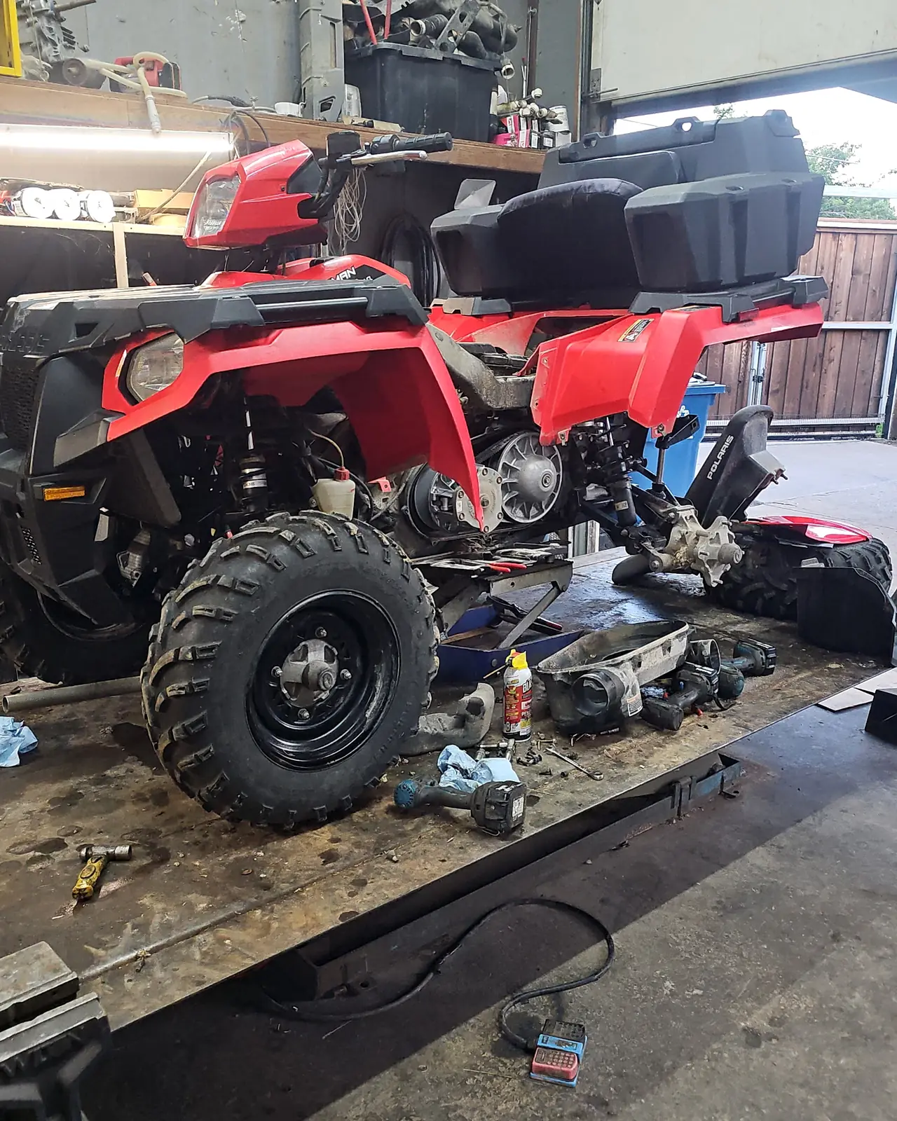 Two red Polaris Sportsman ATVs open on the shop lift mid-service with the clutch covers off